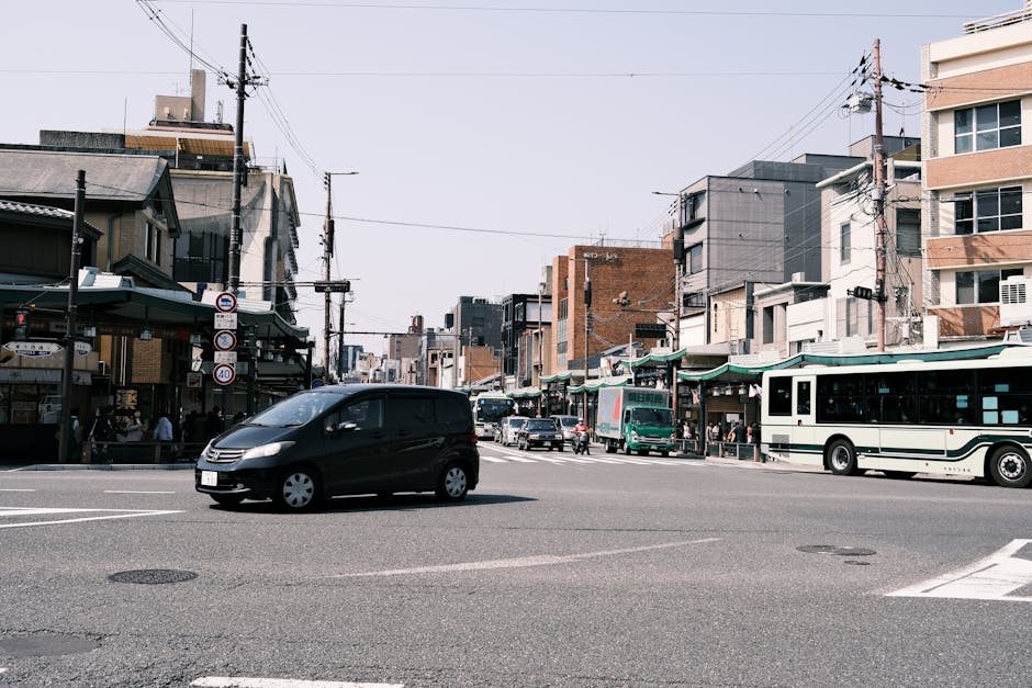 Street view of a bustling intersection in Kyoto, Japan. Features cars and buses in a lively urban setting.