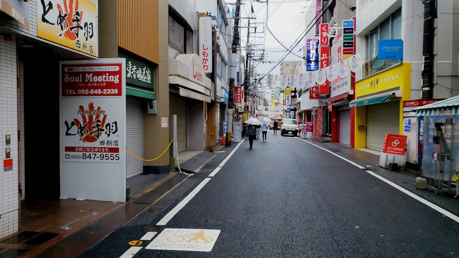 A bustling street in Fukuoka, Japan, featuring local shops and people on a rainy day.