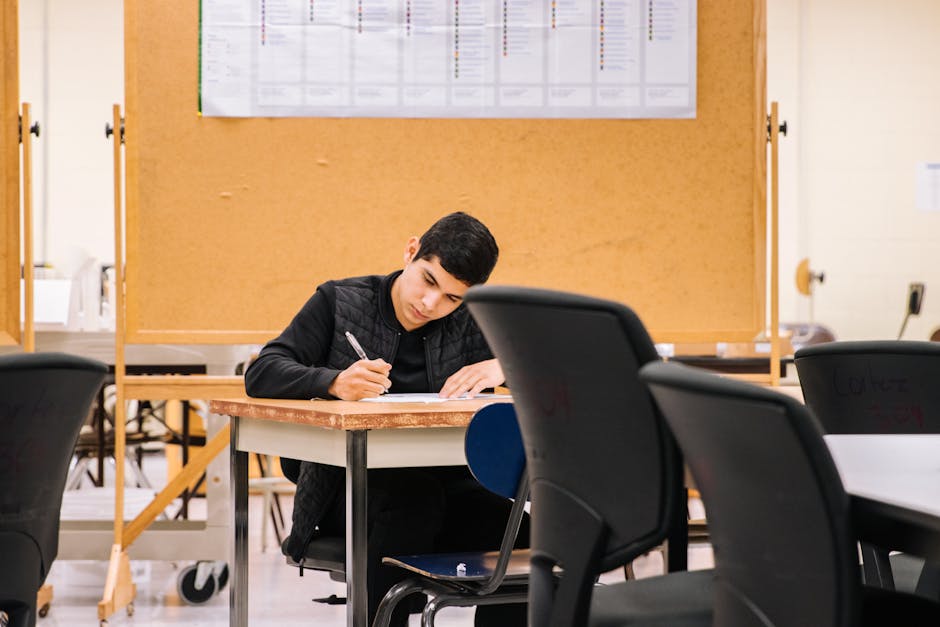 Young man focused on writing in a classroom, ideal for education concepts.