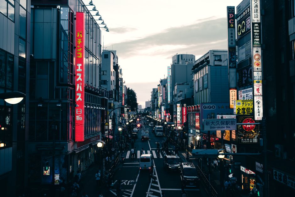 Street view in Tokyo's downtown district filled with neon signs and traffic during twilight.