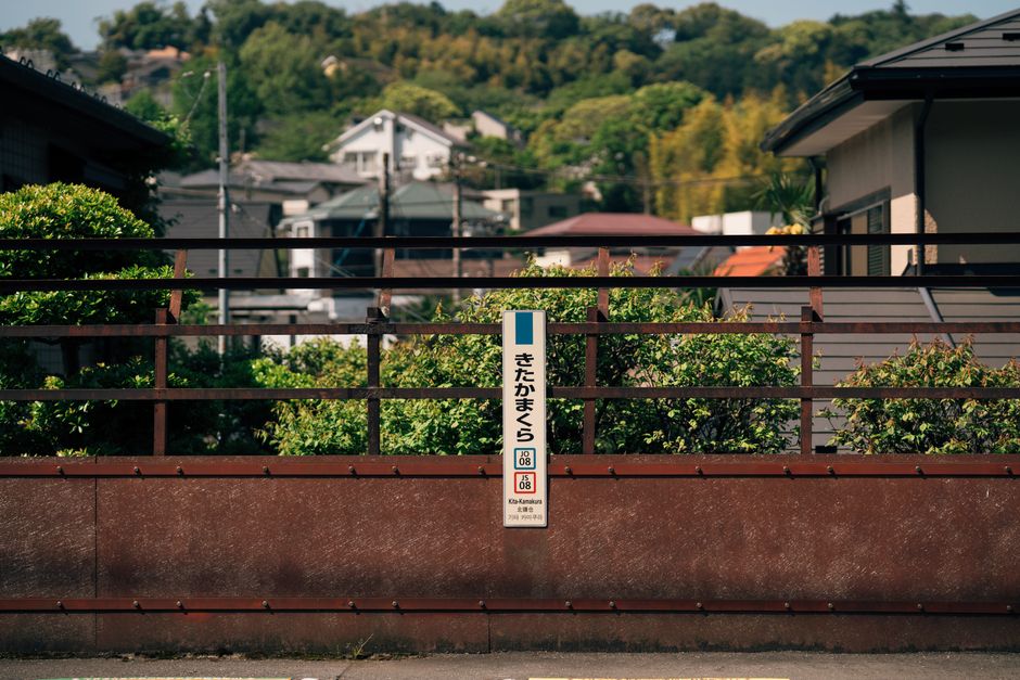 A sign at Kita Kamakura station, surrounded by lush greenery, under a clear sky in Japan.