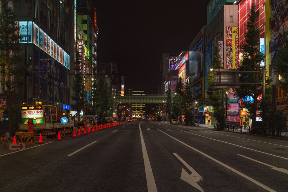 Bustling Tokyo street at night with illuminated buildings and empty road in Chiyoda City.