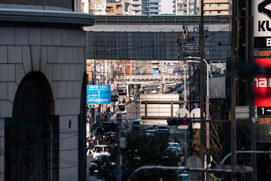 Street scene in downtown Osaka with traffic and urban life beneath a clear sky.