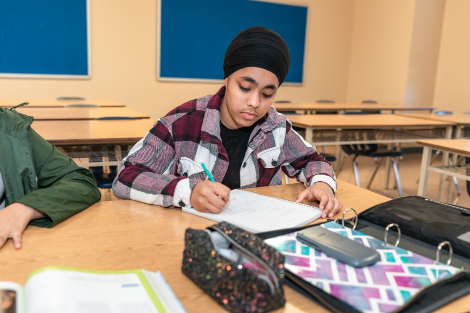 Teenage student writing at a desk in a classroom, focusing on learning and education.