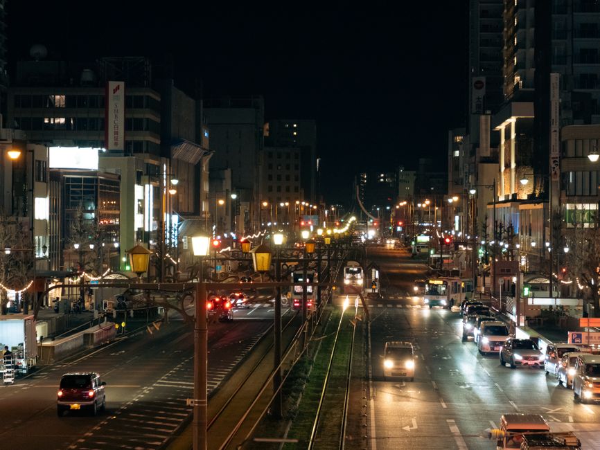 A bustling night scene of Toyohashi's illuminated city street, capturing vibrant urban life.