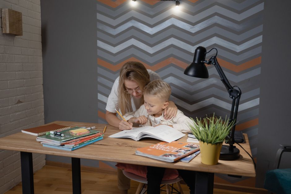A mother assists her son with homework at a desk, fostering a learning environment.